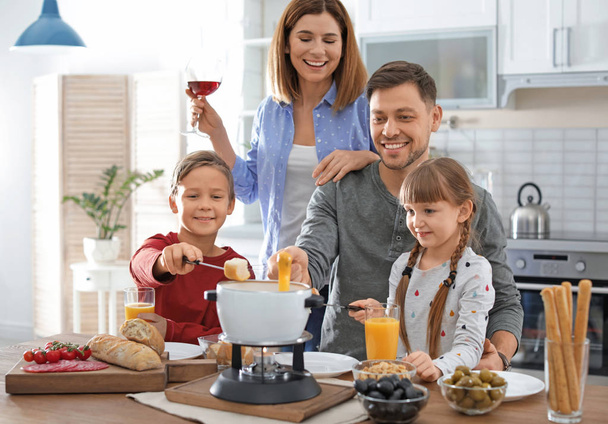 Happy family enjoying fondue dinner at home - Foto, afbeelding
