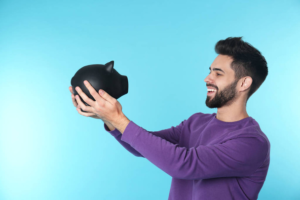 Happy young man with piggy bank on color background. Money saving - Фото, зображення