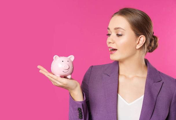 Happy businesswoman with piggy bank on color background. Money saving - Photo, image