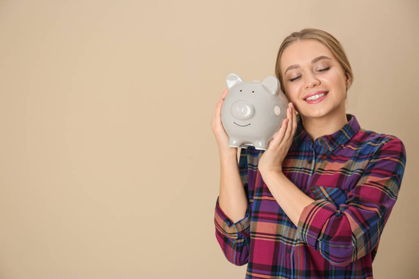 Happy young woman with piggy bank and space for text on color background. Money saving - Zdjęcie, obraz