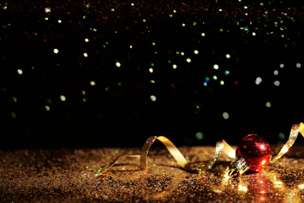 Golden glitter, Christmas ball and streamer against black background. Space for text - Foto, Imagem