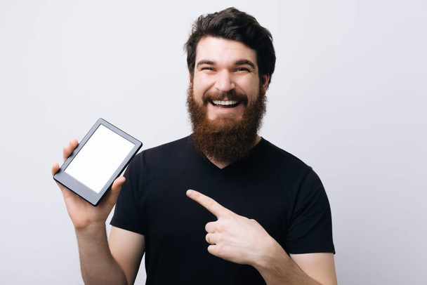 Retrato de um homem barbudo sorridente apontando o dedo em branco tablet tela branca do computador
 - Foto, Imagem
