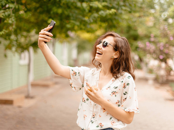 Ritratto di una giovane donna allegra che prende selfie fuori in strada estiva
  - Foto, immagini