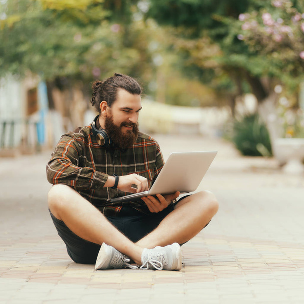Молодой красивый фрилансер сидит на улице в свободное время с новым современным ноутбуком
 - Фото, изображение