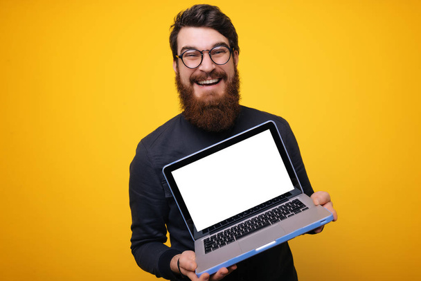 Boldog ember, a szürke póló találat laptop számítógép képernyőjén, a kamera, mint sárga háttérrel - Fotó, kép