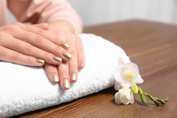 Woman with gold manicure on rolled towel at table, closeup. Nail polish trends - Fotoğraf, Görsel
