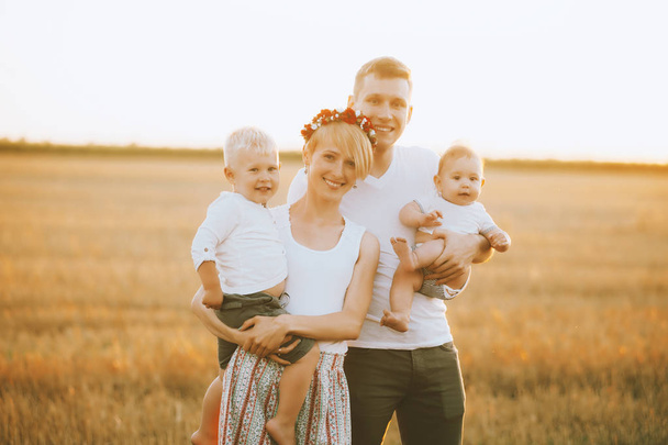 Young happy family walking outdoor, in field on sunset. Parents hold children on hands and rejoice. They are happy together - Фото, зображення