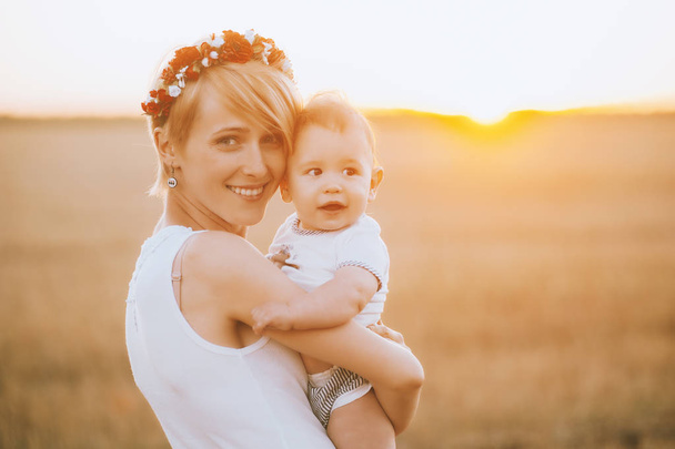 Young  woman with her little son,  smiling and hugging on nature in field at sunset. Family bond concept. - Photo, image