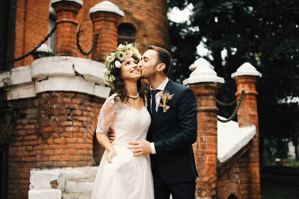 Όμορφο γαμήλιο ζεύγος στέκεται κοντά στο παλιό κάστρο τούβλο, husbband αγκαλιές και φιλιά τη γυναίκα του - Φωτογραφία, εικόνα