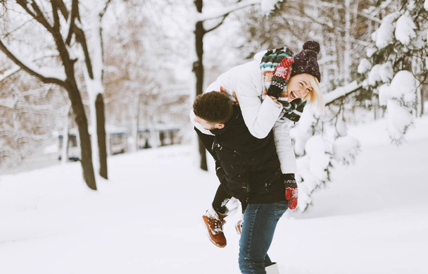 A pretty couple, boy and girl, having fun in snow, he lift up his girlfriend on shoulder - Photo, image