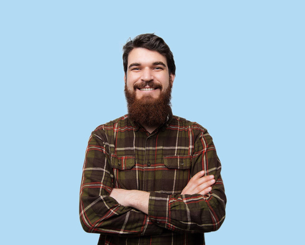 Photo of happy fashionable handsome bearded man in brown shirt crossing hands, smiling and looking at camera - Foto, imagen