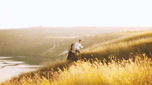 Foto de bonito casal caminha na natureza, no topo da colina perto do lago ou rio
 - Foto, Imagem