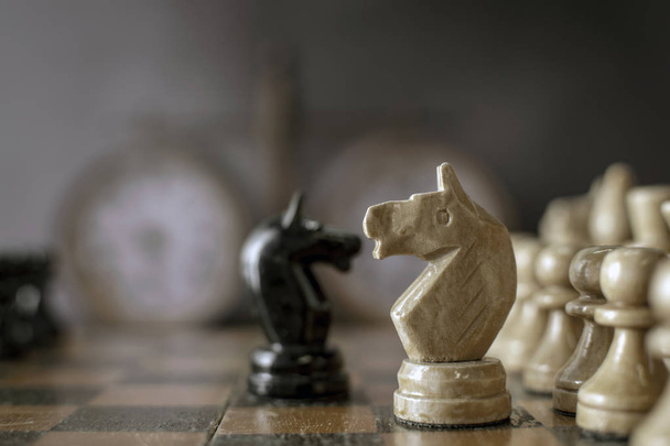 Старая шахматная доска с фигурами и винтажными шахматными часами на размытом фоне. Красивый концептуальный фон для дизайна и текста с мягким светом. Селективный фокус
 - Фото, изображение