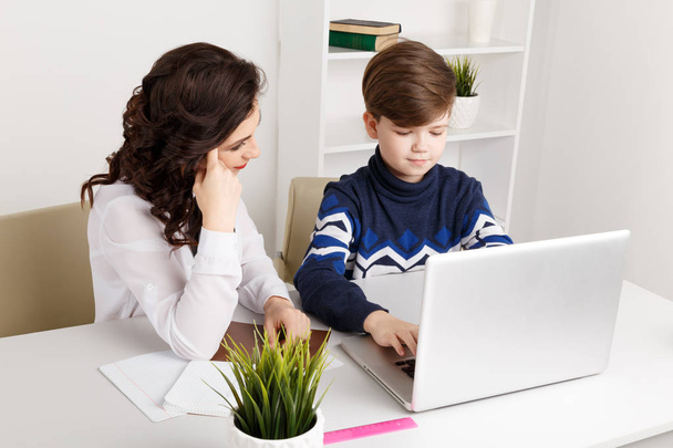 Tutor and the boy doing homework in the white classroom. Typing homework on a laptop. - Foto, Imagem