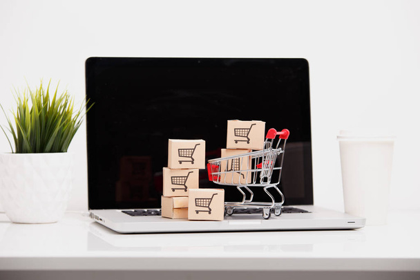 オンライン ショッピング e コマースや配信サービス概念: ショッピング カートとカートンの紙やノート パソコンのキーボードのロゴをトロリー、インターネット小売業者サイトから顧客注文の事を示しています - 写真・画像