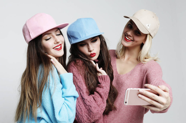 Three happy best girlfriends wearing sweaters and caps making selfie on smartphone. - Foto, Imagen
