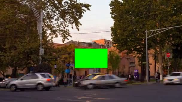 Zeitraffer-Video. Werbetafel mit grünem Bildschirm mitten im herbstlichen Stadtbild mit verschwommenen Fußgängern und Autos. Kamera nähert sich - Filmmaterial, Video