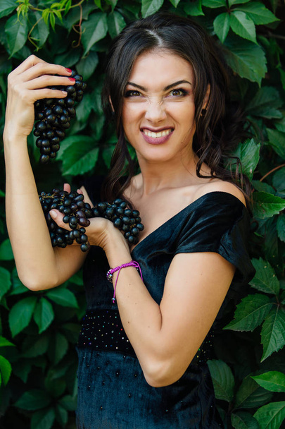 Portrait of young sexy brunette biting black grapes. - Фото, зображення