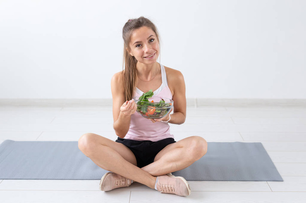 Gesunder Lebensstil, Menschen und Sportkonzept - Yoga-Frau mit einer Schüssel Gemüsesalat nach dem Training vor weißem Hintergrund - Foto, Bild