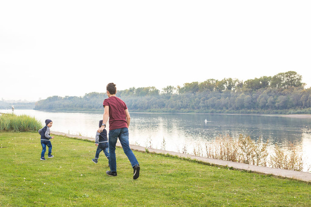 Childhood, family concept - father playing with two sons near the lake - Foto, Imagen