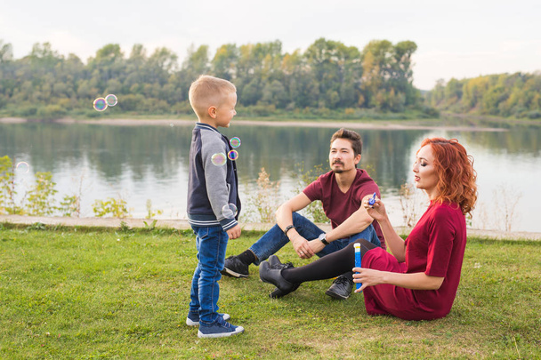 Family and nature concept - Mother, father and their child playing with colorful soap bubbles - Fotografie, Obrázek