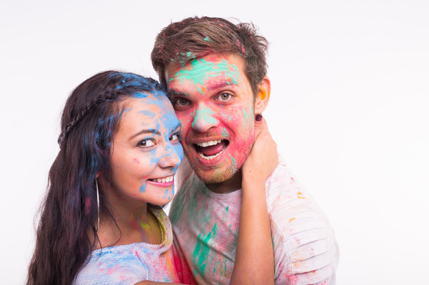 Vakantie, holi en mensen concept - lachende grappige vrouw en man poseren met veelkleurige poeder op hun gezichten op witte achtergrond - Foto, afbeelding