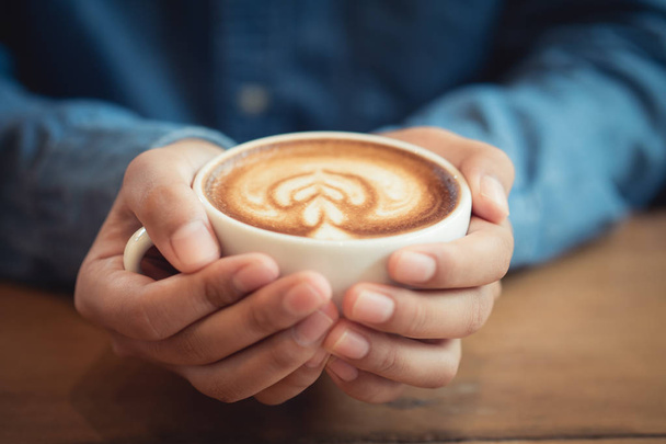 Man hands holding a cup of coffee on wooden table - Foto, imagen