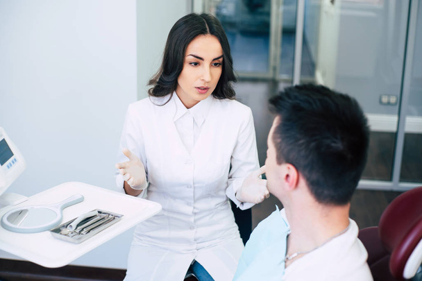 What are your complaints? A dentist on her work in the hospital is sitting right in front of a patient in medical clothes and asking about his complaints. - Foto, Imagem