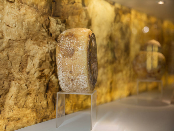Forma de queijo redondo exibido em um pedestal transparente em uma loja
 - Foto, Imagem
