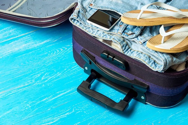 Open suitcase with travel accessories on blue wooden table with copyspace. - Valokuva, kuva