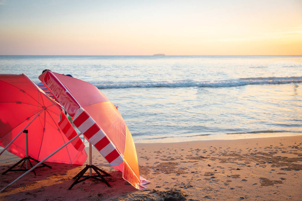 Red umbrella on the beach among  sunset on the sea. - Фото, изображение