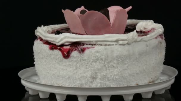 Mooie stijlvolle zoete verse witte cake met cherry jam versierd op de top met room en kokoschips op een zwarte achtergrond. - Video