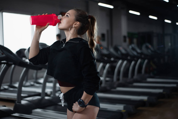 Girl after a workout drinking water in the gym - Fotoğraf, Görsel