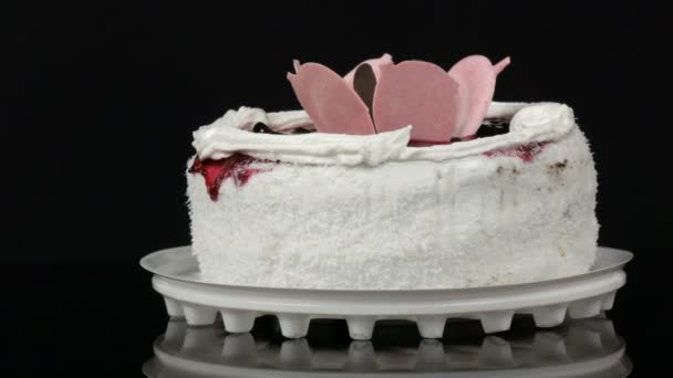 Красивий стильний солодкий свіжий білий торт з вишневим джемом, прикрашений зверху кремом та кокосовими чіпсами, обертається на чорному тлі
. - Кадри, відео