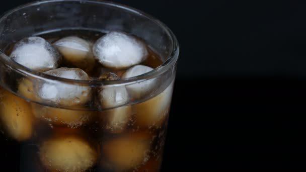 Burbujas de cola fría en un vaso largo transparente con hielo sobre un fondo negro
. - Metraje, vídeo