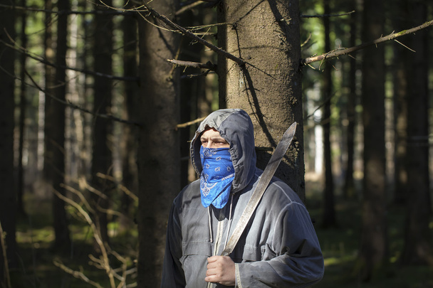 man met een machete in het bos leunend tegen boom - Foto, afbeelding