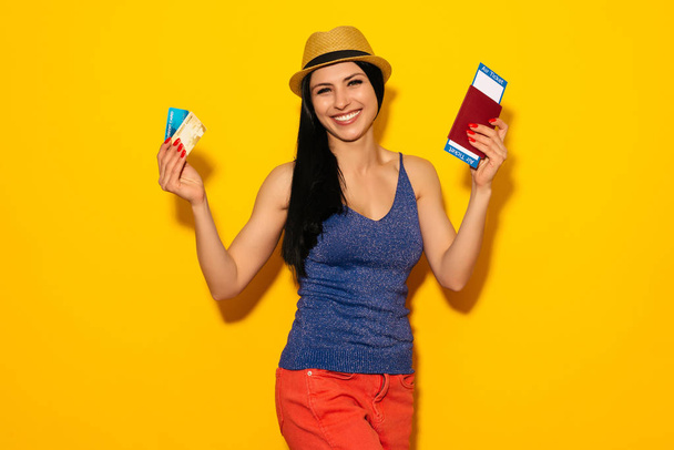 Młody student uśmiechający się trzymając bilet wydać paszportu i karty kredytowej na białym tle na żółtym tle. - Zdjęcie, obraz