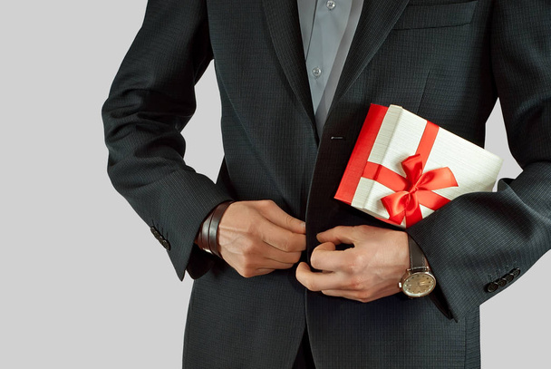 A man in a suit holds a gift box in his hands. Box with a red ribbon and a bow. - Fotografie, Obrázek