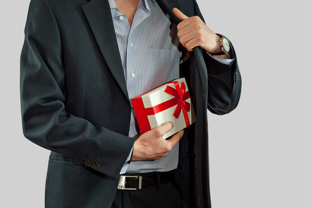 Un homme en costume tient une boîte-cadeau dans ses mains. Boîte avec un ruban rouge et un arc
. - Photo, image