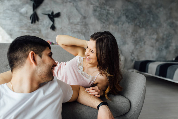 Laughing young people in pajamas playfully posing at sofa. Happy couple smiling in morning - Foto, Imagen