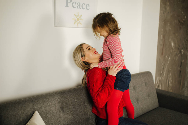 Little girl in red tights with mom in red sweater. Happy family at home. Daughter hug her mother - Foto, Bild