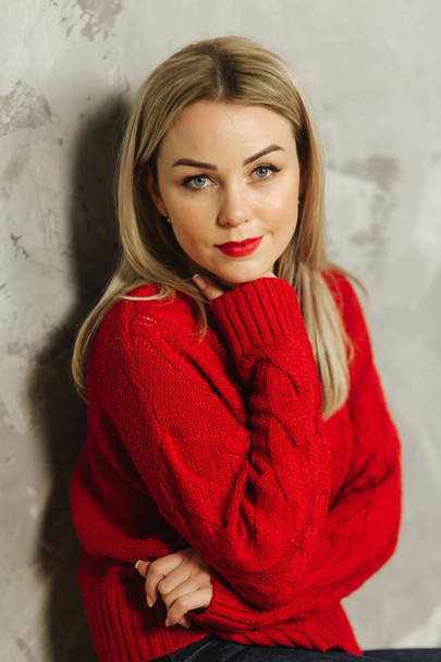 Beautiful woman in red sweater and red lips at home. Happy blond hair lady - Fotó, kép