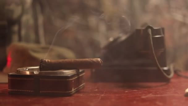 Primer plano de un cigarro cubano y cenicero sobre la mesa de madera. Mesa de comandante dictador comunista en cuarto oscuro. Concepto de mesa de trabajo del general del ejército. Decoración de obra
 - Imágenes, Vídeo