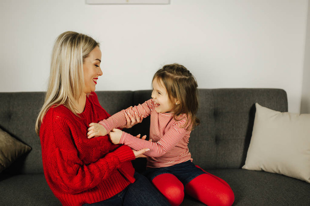 Mom and daughter play at home. Little girl tickle her mother. Happy family spend time together. Blond hair woman - Photo, Image
