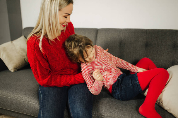 Mom and daughter play at home. Little girl tickle her mother. Happy family spend time together. Blond hair woman - Photo, Image