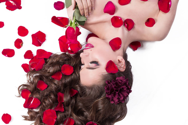 young woman with rose lying among rose petals - Foto, afbeelding