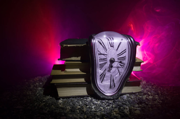 Time Concept. Distorted soft melting clock on the old books. With dark toned foggy background. Selective focus - Photo, Image