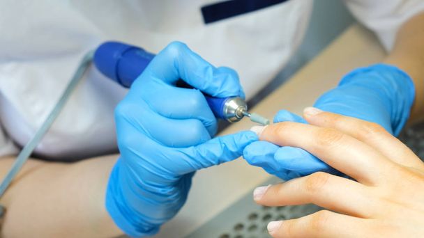 Manicurist, nail artist handles nails with manicure milling cutter. Beauty service, nail salon, health care and cosmetics. Close up. - 写真・画像