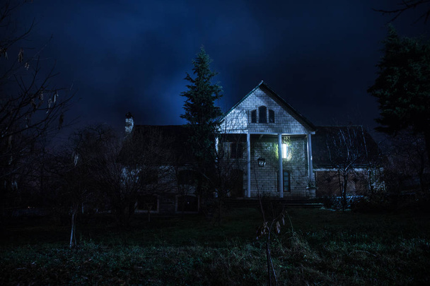 Régi ház egy szellemmel az erdőben éjszaka, vagy elhagyott kísértetjárta horror ház ködben. Régi misztikus épület a halott fák erdejében. Fák éjjel a holddal. Szürreális fények. Horror Halloween koncepció - Fotó, kép