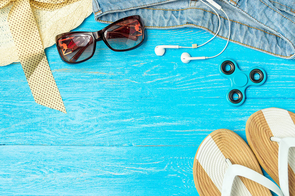 Marco elegante mujer sombrero de paja zapatillas jeans gafas de sol sobre fondo de madera azul, espacio de copia para el texto, vacaciones de verano
. - Foto, imagen